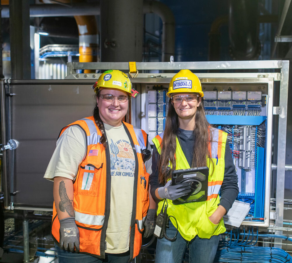 Two employees standing in front of a panel smiling at the camera.