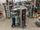 Two technicians work on large electrical control panels with exposed wiring and components inside an industrial manufacturing facility.
