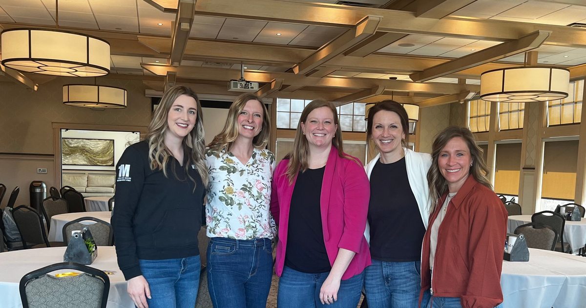 Five women posing for a picture in a large conference room.