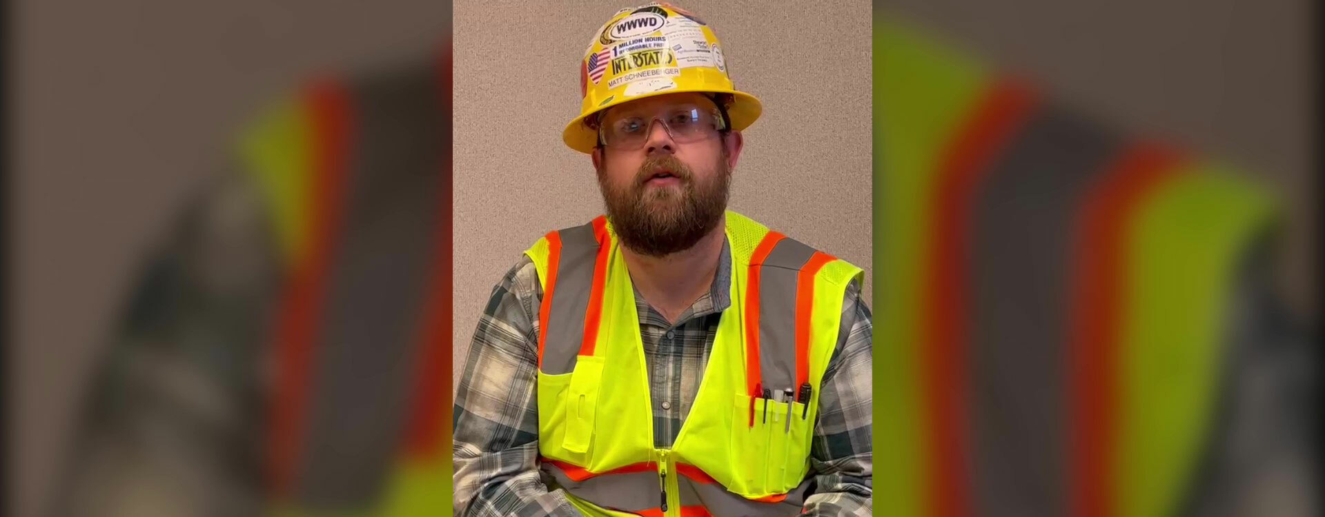 man sitting wearing a hard hat, safety glasses, and high vis vest