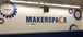 white wall with blue gear decals and blue and orange words that say makerspace