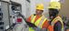 tow men in high visibility vests looking at a panel outside a building