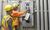 Two men wearing PPE gear working on a breaker box.