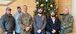 Six men standing in front of a decorated Christmas tree
