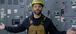 Man with a hardhat standing in an electric room with his arms out at his sides.