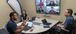 Three people in person conducting a meeting with four people joining online.
