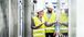 Man and woman wearing yellow safety vests viewing something on a tablet.