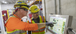 Two men wearing yellow and orange PPE gear pointing at a monitor.