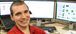 Man in a red shirt smiling in front of computer monitors.