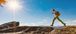 A photo of a person outdoors, mid-jump on a rocky surface with a bright blue sky and sunshine overhead