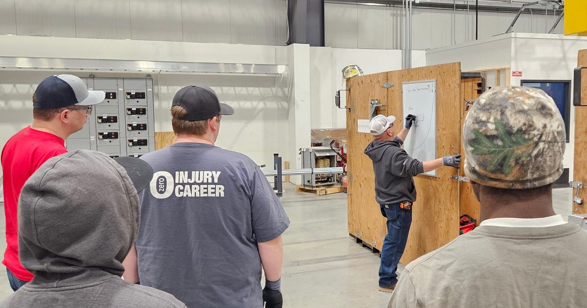 Four people in a manufacturing shop with someone teaching three of them by drawing on a whiteboard