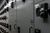 A narrow industrial electrical room lined with tall gray control panels on both sides. Each panel has black handles, switches, indicator lights, and digital keypads.