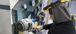An electrician/electrical worker wearing protective gear (PPE) and a hard hat is using a wrench on an instrument or motor in an industrial facility