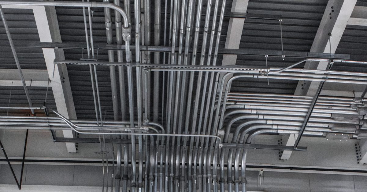 Vertical electrical conduits neatly routed and supported along a wall and ceiling inside an industrial facility, demonstrating a clean, organized installation.