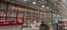 Interior of a high‑bay warehouse under construction with tall pallet racks, bright overhead lights, and red scissor lifts on the concrete floor.