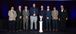 Eight Interstates team members stand on stage in formal attire with a white eagle trophy displayed on a pedestal in front of them at an awards event.