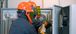 Two people in arc flash suits looking into an electrical box.