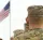 Soldiers in camouflage uniforms saluting near an American flag.