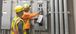 Two men wearing PPE gear working on a breaker box.