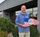 Man standing in front of a building holding an award that has the design of the american flag on it.