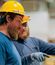 Two men in yellow safety hats and goggles having a discussion.