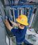 A man in a blue shirt and yellow hard hat working on some wiring.