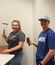 Two women smile while painting a room, one holding a paint roller and the other holding a brush.