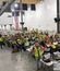A large group of workers in safety vests gathered in a warehouse-style space, seated at tables and waving for a group photo during a safety recognition event.