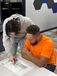 Two coworkers review a printed technical drawing at a table in an office, with one pointing to a specific detail on the plan.
