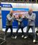 Three people pose in front of a booth at a trade show, each holding up a boxing stance with fists raised.