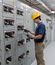 Worker wearing a hard hat, safety glasses, and gloves inspects electrical switchgear inside a modular electrical building.