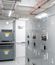 Interior view of a modular electrical building featuring a long row of gray electrical switchgear and overhead cable trays.