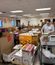 People organize boxes, food items, and supplies inside an office space, preparing donations or materials on tables and carts.