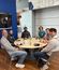 A small group of people sits around a table in a casual meeting space, engaged in conversation.