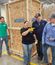 Four workers in a warehouse smile and stand together in front of large wooden shipping crates marked with the logo.