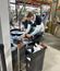 A person works on equipment inside an industrial facility, using tools at a workstation surrounded by machinery and materials.