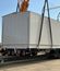 Large modular electrical building being lifted by a crane with multiple straps above a transport trailer.