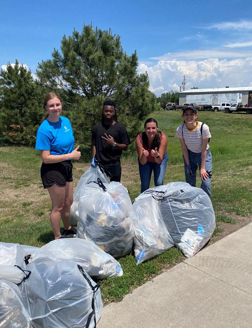 Interns gathered outdoors, holding large garbage bags and smiling.