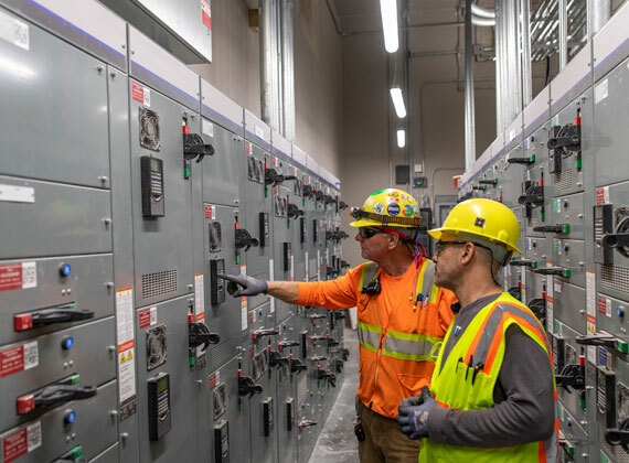 Two electricians looking at the front of a panel.