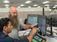 Two employees review a tables of information on several monitors.