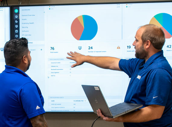 Two employees review cybersecurity software on a large monitor.