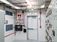 Interior view of a modular electrical building featuring rows of electrical switchgear, overhead cable trays, ventilation systems, fire safety equipment, and an emergency exit door.