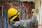 A worker in a yellow hard hat and gray hoodie is wiring a large electrical control panel filled with neatly bundled multicolored cables.