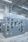 A large gray industrial electrical control panel stands indoors with many switches, handles, and warning labels on its doors. Numerous metal conduits run from the top of the panel up to the ceiling in a well-lit, clean industrial space.
