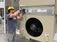 Worker wearing a hard hat, safety glasses, and gloves installs or adjusts a component on a large industrial HVAC unit inside a manufacturing facility.