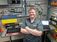 man in front of wires and a laptop smiling with his arms folded and an Interstates shirt on
