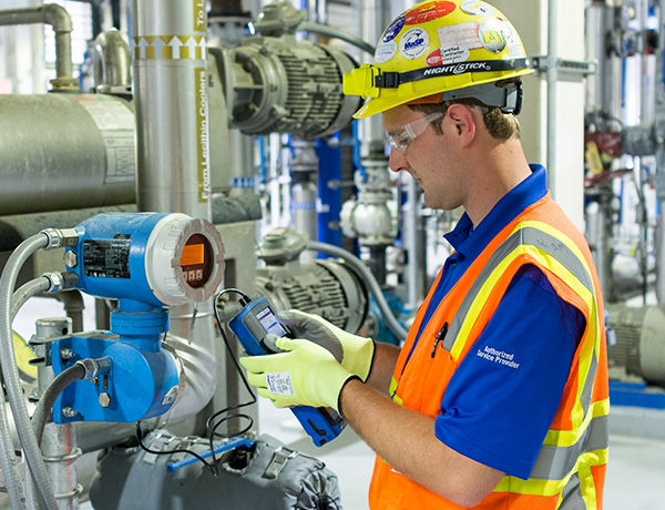 An employee wearing a hard hat and vest checks maintenance.