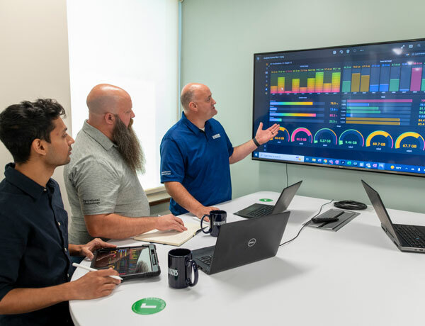Three employees viewing a dashboard on a large computer monitor.