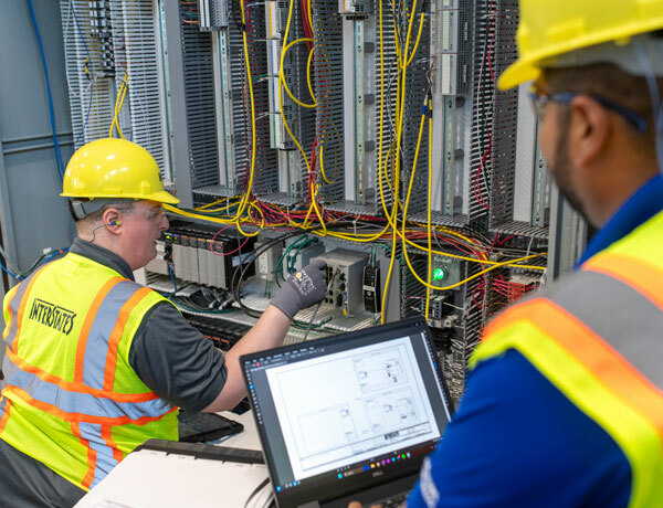 One employee reviews the network configuration while another employee adjusts the equipment.