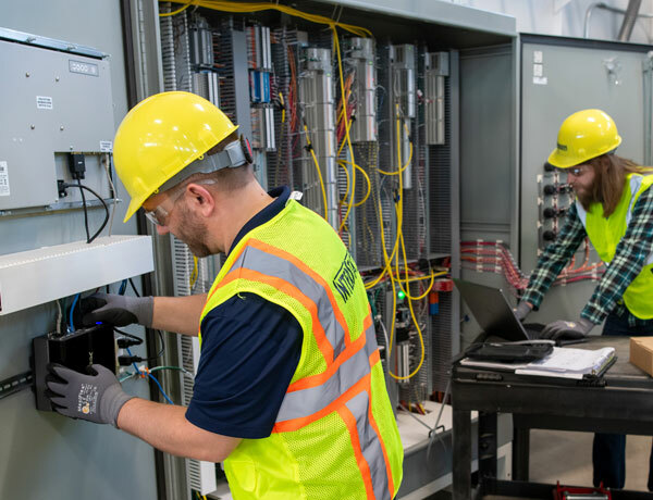One employee works on an edge device while another monitors the network from a control panel.